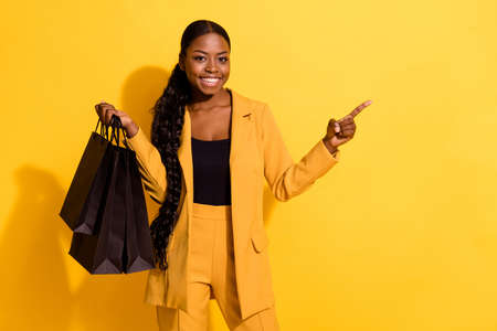 Portrait of beautiful trendy cheerful chic girl holding buyings showing copy space isolated on bright yellow color backgroundの写真素材