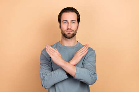 Photo of young man conflict crossed arms show rule forbidden signal isolated over beige color...