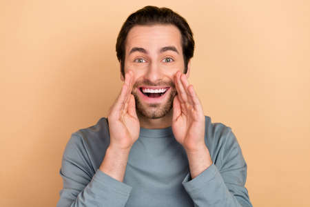 Photo of young excited guy arms near mouth yell advertising discount isolated over beige color backgroundの写真素材