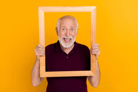 Photo of cheerful senior man have fun fool tongue-out shoot picture isolated over yellow color backgroundの写真素材