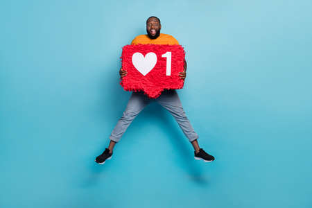 Photo of funny excited guy dressed orange t-shirt jumping holding feedback pinata isolated blue color backgroundの写真素材