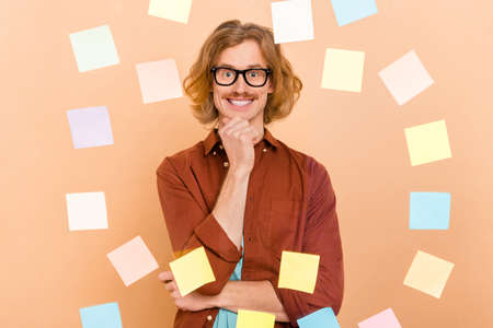 Portrait of attractive cheerful minded red-haired guy choosing memo card wall solution isolated over beige pastel color backgroundの写真素材