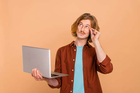 Portrait of handsome minded trendy red-haired guy using laptop deciding isolated over beige pastel...