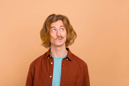 Portrait of attractive funky bewildered red-haired guy overthinking solution isolated over beige...