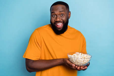 Portrait of attractive cheerful guy eating popcorn watching tv series free time isolated over bright blue color backgroundの写真素材