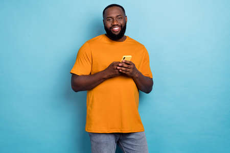 Photo of cheerful sweet guy dressed orange t-shirt communicating modern gadget isolated blue color backgroundの写真素材