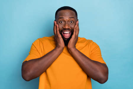 Photo of funky shocked guy dressed orange t-shirt smiling arms cheeks isolated blue color backgroundの写真素材