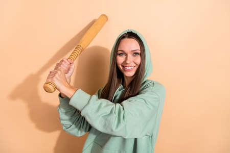 Portrait of attractive confident cheerful girl holding bat hit play isolated over beige pastel color...