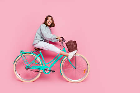 Full body profile side photo of young cheerful lady have fun playful hobby ride bike isolated over pink color backgroundの写真素材