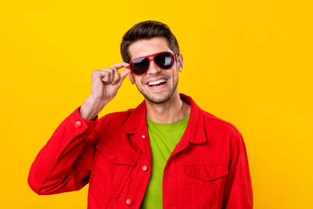 Portrait of attractive cheerful guy touching specs good mood isolated over vibrant yellow color...