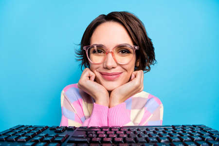 Photo of cute young brunette lady look laptop wear spectacles pink sweater isolated on blue backgroundの写真素材