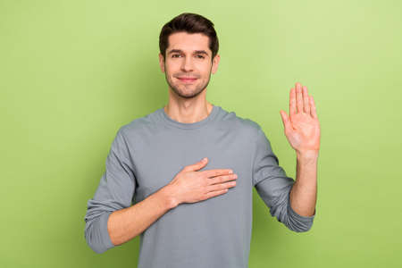 Photo of cute young brunet guy pray wear grey shirt isolated on green color backgroundの写真素材