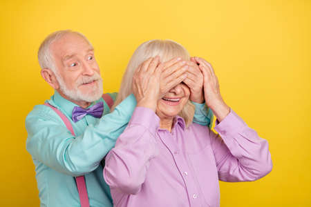 Portrait of two attractive cheerful grey-haired spouses closing eyes preparing gift isolated over bright yellow color backgroundの写真素材