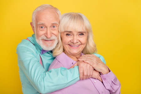 Portrait of two attractive cheerful grey-haired spouses bonding amour isolated over bright yellow color backgroundの写真素材