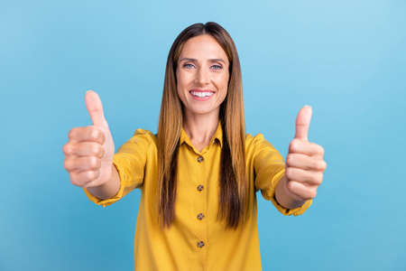 Photo of cool young brown hairdo lady thumb up wear yellow shirt isolated on blue color backgroundの写真素材