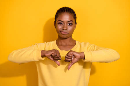 Portrait of attractive skeptic girl showing thumb down dislike no isolated over bright yellow color backgroundの写真素材