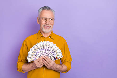 Photo of senior man hold cash wealthy curious look empty space profit isolated over violet color...
