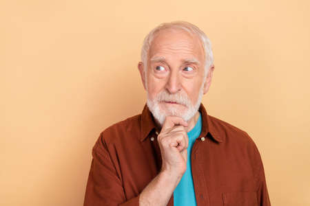 Photo of thinking old grey hairdo man look empty space wear brown shirt isolated on beige color...