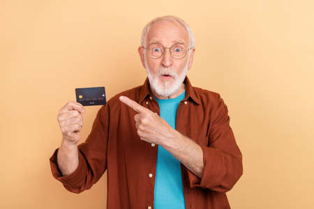 Photo of impressed astonished grandfather promote credit card savings salary isolated on beige color backgroundの写真素材