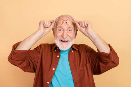 Photo of impressed elder grey hairdo man look camera wear spectacles brown shirt isolated on beige...