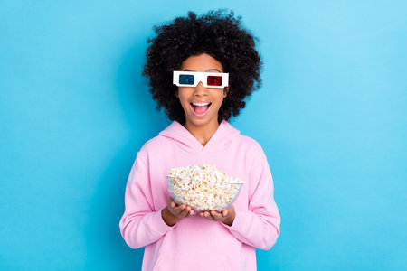 Portrait of attractive cheerful trendy girl holding pop corn watching film having fun isolated over bright blue color backgroundの写真素材
