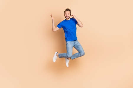 Full length photo of young man jump up tell listen talk mobile communication energetic isolated over beige color backgroundの写真素材
