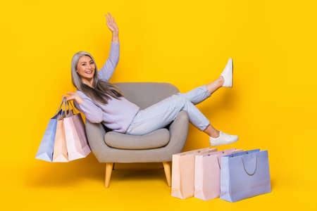 Photo of funny shiny lady pensioner dressed pullover sitting cozy chair rising bargains isolated...