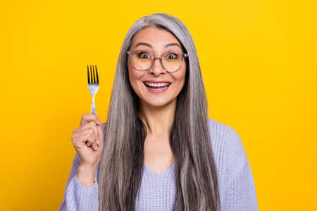 Portrait of cheerful funky amazed grandmother waiting her yummy dessert isolated on yellow color backgroundの写真素材