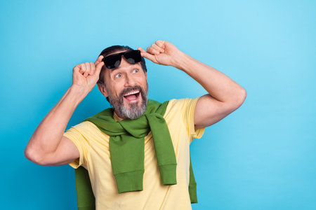 Portrait of impressed positive man hands touch glasses look interested empty space isolated on blue color backgroundの写真素材