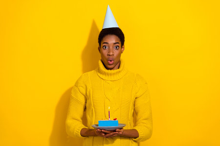 Photo of surprised lady man in knitted jumper make wish receive slice of yummy birthday cake isolated on yellow color backgroundの写真素材