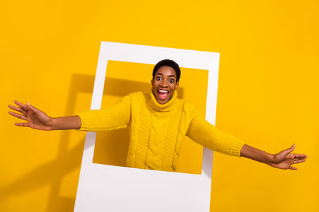 Portrait of attractive cheerful funky girl coming out frame comfort zone isolated over bright yellow color backgroundの写真素材