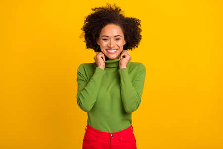 Portrait of attractive cheerful wavy-haired girl wearing warm pullover isolated over bright yellow color backgroundの写真素材