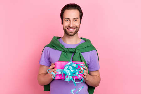 Photo of nice millennial beard man hold present wear t-shirt pullover isolated on pink color backgroundの写真素材