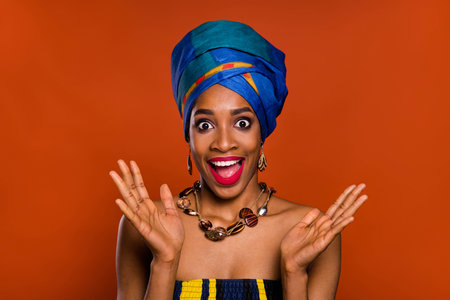Photo of funny impressed woman wear ethnic turban smiling rising arms open mouth isolated red color...