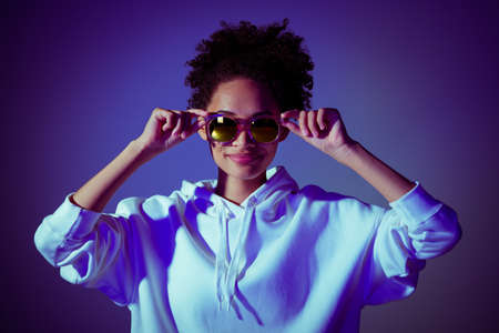 Photo of cool adorable lady dressed hoodie arms dark eyewear smiling isolated blue color background