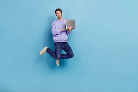 Full length body size view of attractive cheerful trendy guy jumping using laptop isolated over bright blue color backgroundの写真素材