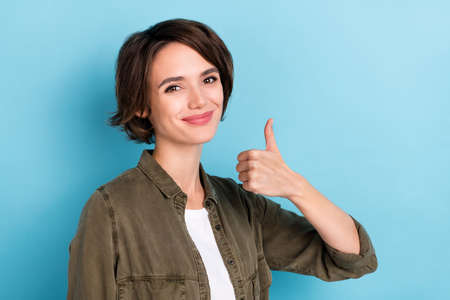 Photo of cool young brunette business woman thumb up wear khaki shirt isolated on blue color backgroundの写真素材