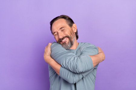 Photo of cute good looking positive male hug himself feeling warm express self love isolated on violet color backgroundの写真素材