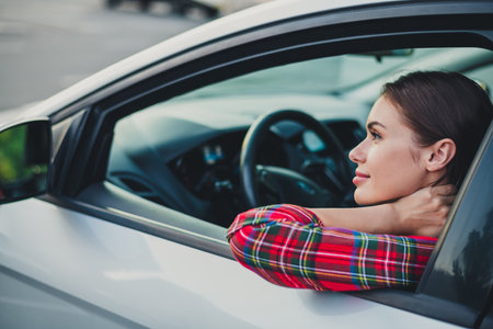 Profile side view portrait of attractive cheerful girl driving car looking at mirror on parking enjoying mood outdoorsの写真素材