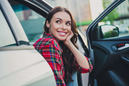 Portrait of attractive cheerful wavy-haired girl passenger sitting in auto waiting husband shopping on parking outdoorsの写真素材