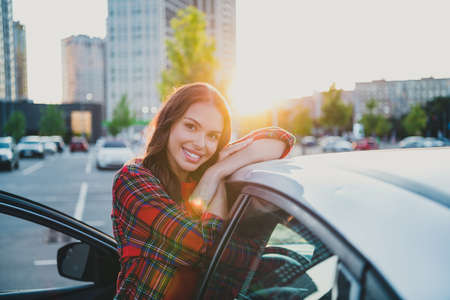 Portrait of attractive cheerful wavy-haired girl driver resting enjoying sunset evening free time on parking outdoorsの写真素材