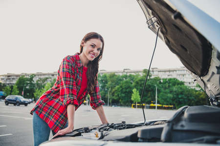 Portrait of attractive cheerful wavy-haired girl taxi service driver checking tech part on car before trip on parking outdoorsの写真素材
