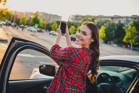 Portrait of attractive cheerful wavy-haired girl making taking photo of sunset sun set on parking...