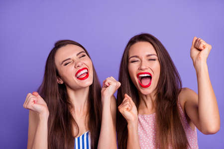 Photo of sweet lucky two best friends dressed summer clothes rising fists screaming isolated purple color backgroundの写真素材