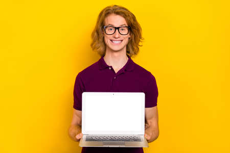 Photo of cute millennial red hairdo guy show laptop wear eyewear purple polo isolated on yellow...