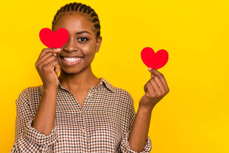 Photo of funny adorable lady dressed checkered shirt holding two little hearts cover eye isolated yellow color backgroundの写真素材