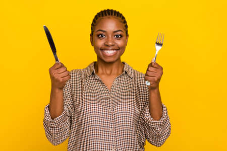 Photo of positive funny lady dressed checkered shirt holding silver fork knife isolated yellow color backgroundの写真素材
