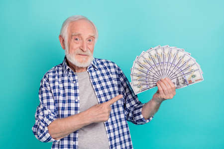 Photo of cute handsome mature man showing his wealth holding money dollars isolated on teal color backgroundの写真素材