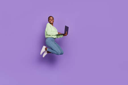Full body picture of cheerful young lady browsing laptop chatting with friends isolated on violet...