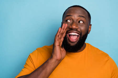 Photo of excited funky guy dressed orange t-shirt arm mouth making announcement looking empty space isolated blue color backgroundの写真素材